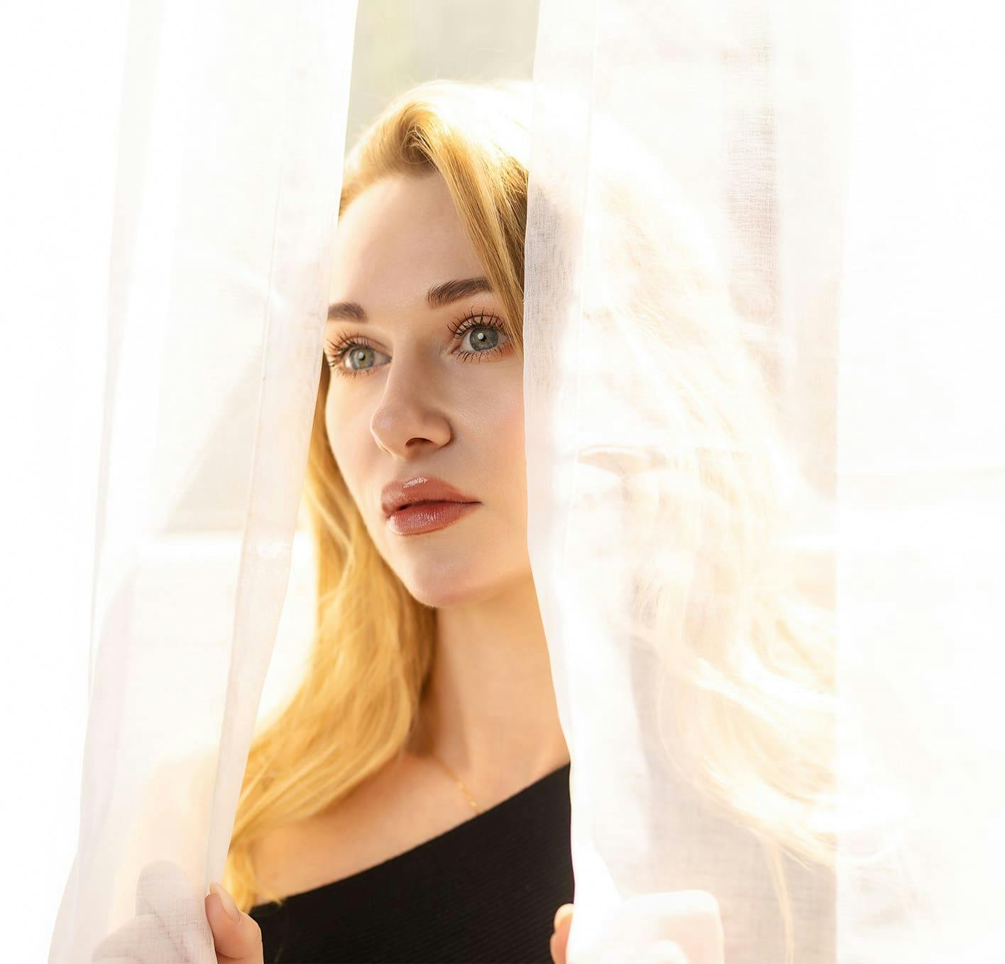 woman looking through thin curtains