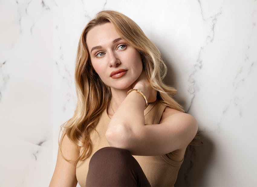 woman leaning against wall with her hand rubbing her neck
