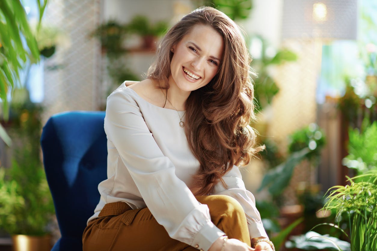 woman with thick brow hair smiling with a palm tree background