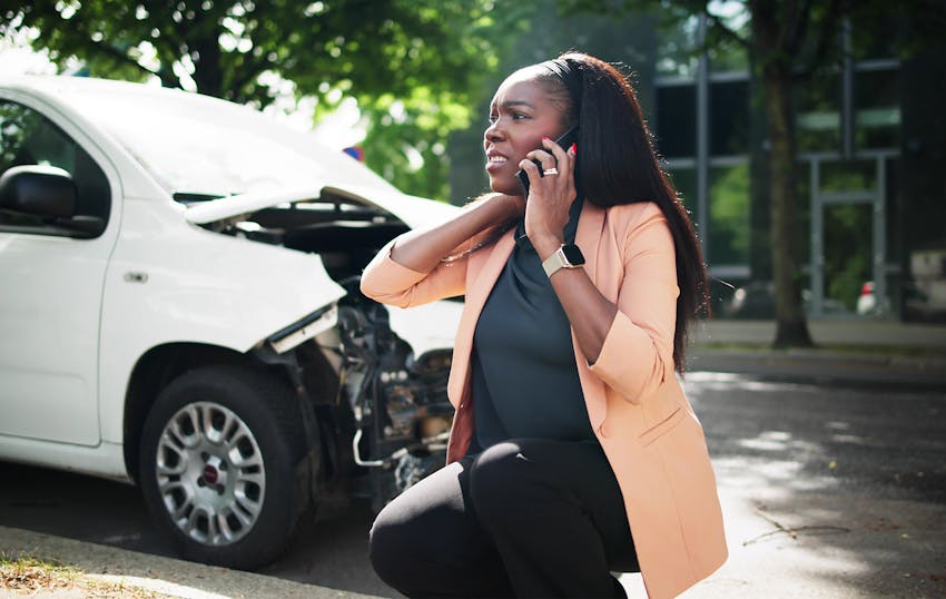 woman on the phone next to a car with a crumpled front end