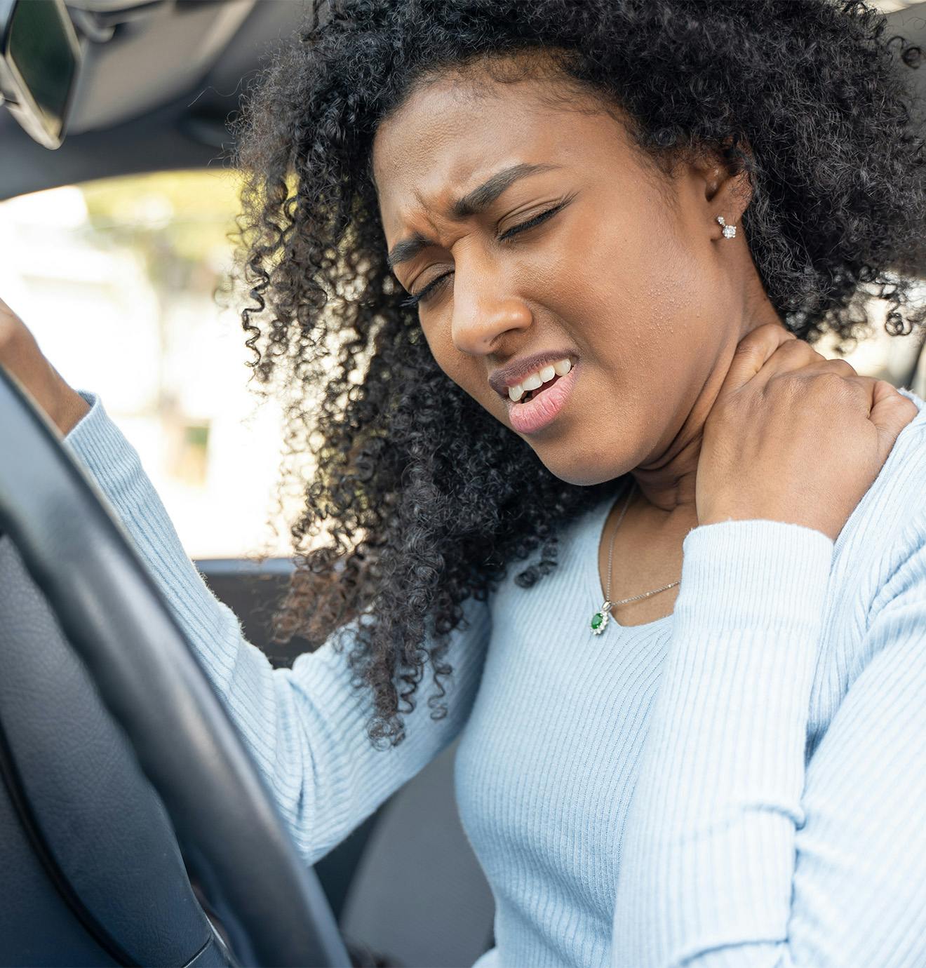 woman holding her neck in pain while sitting in a car
