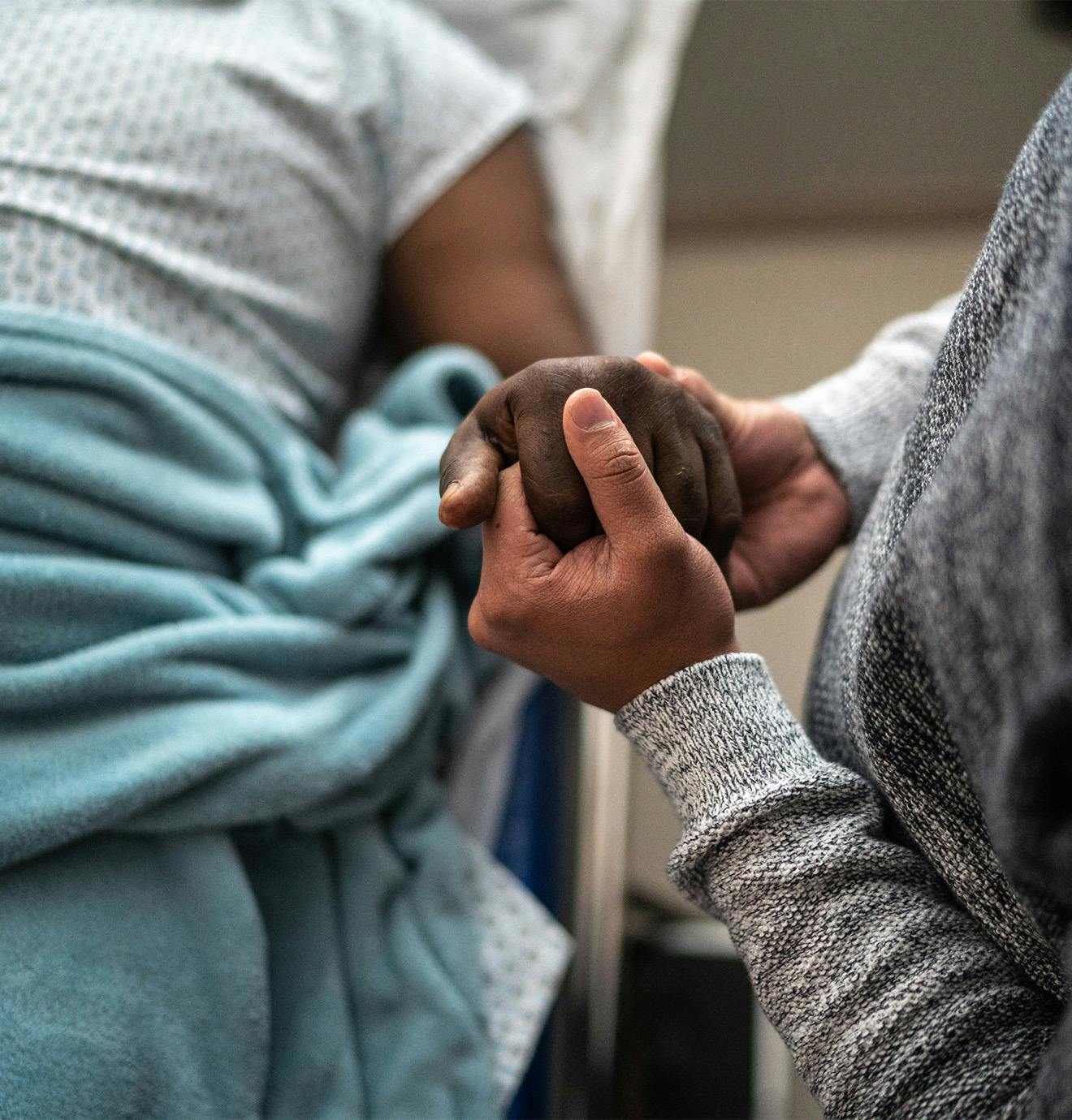 person in a hospital bed holding someone's hand