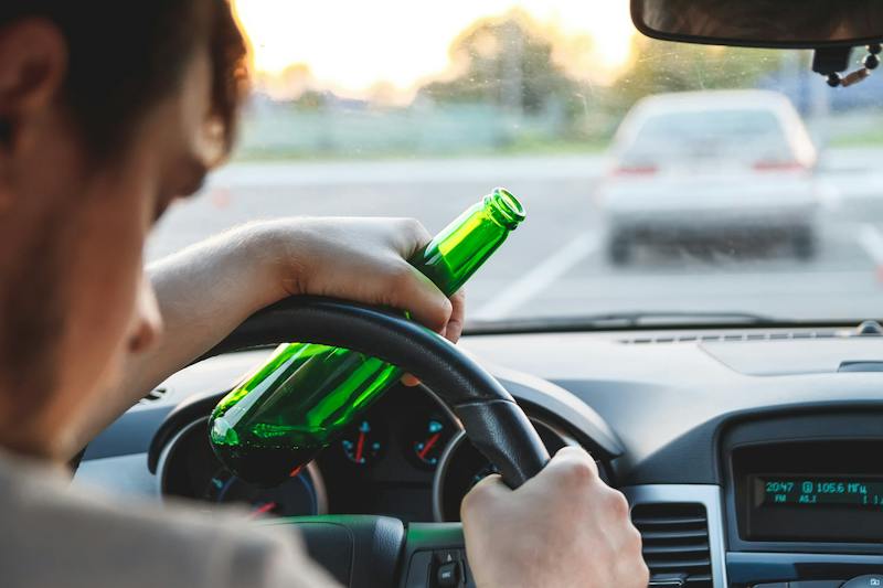 man driving while holding a beer bottle