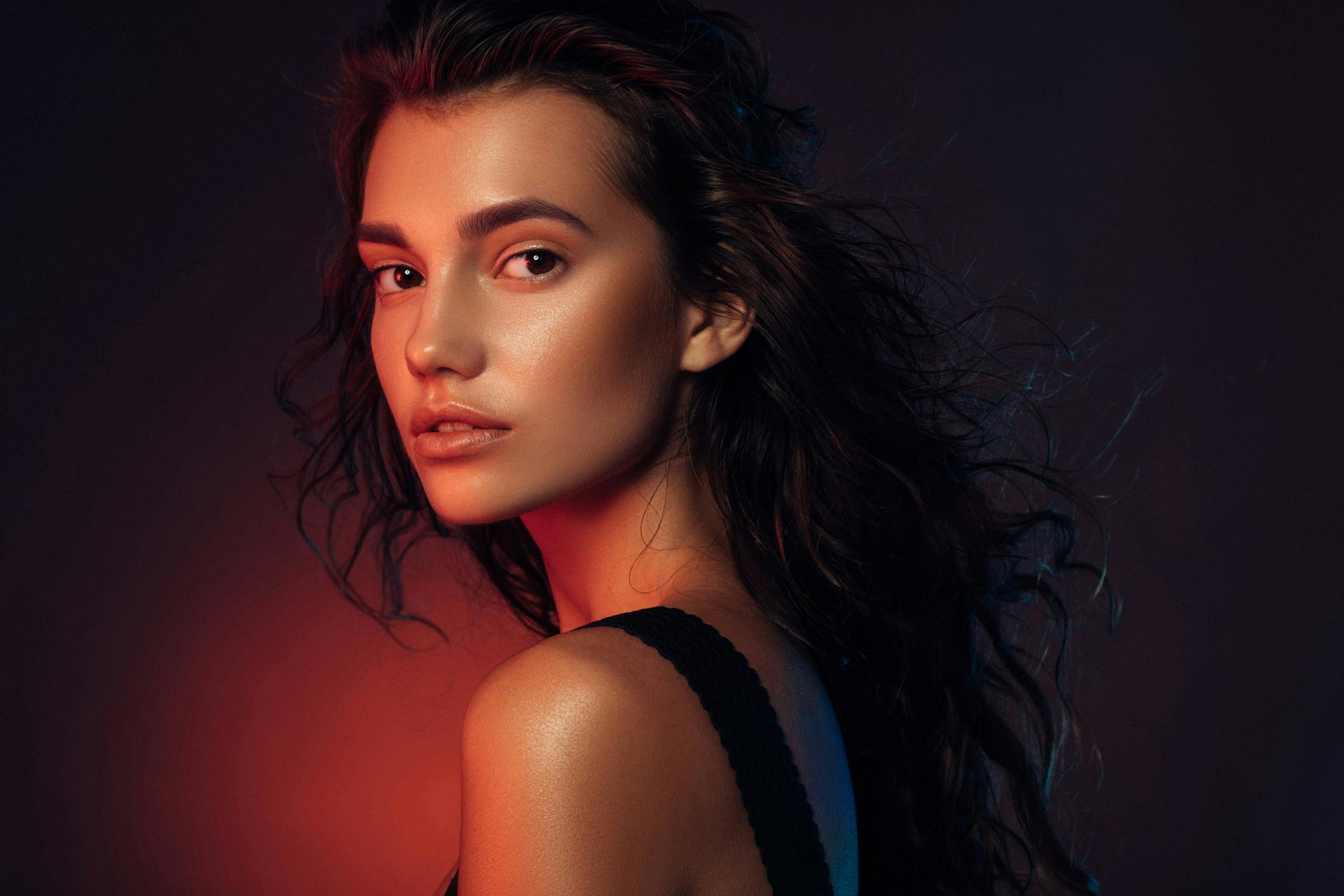 A youthful woman is having her portrait taken. the image is moody with a glow on her face and body.