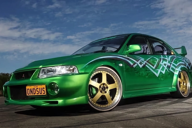 Lowered metallic green Mitsubishi Lancer Evolution with gold TE37-style wheels, custom white vinyl graphics, and ONDSUS license plate