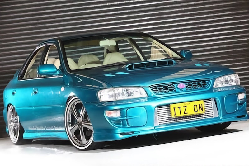 Lowered teal Subaru Impreza WRX with custom front bumper, chrome wheels, cream interior, and ITZ ON license plate