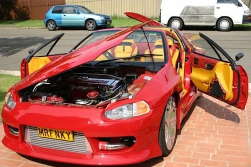 Red Honda CRX with all doors and hood open showing custom yellow interior, chrome wheels, and MRFNKY license plate