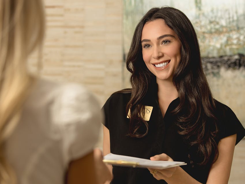 woman smiling, handing another woman paperwork
