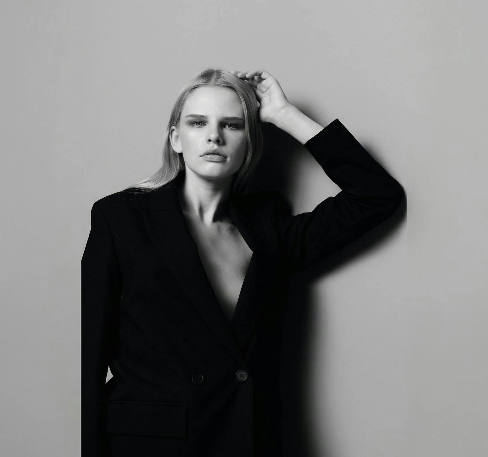 woman in suit jacket leaning on wall in black and white