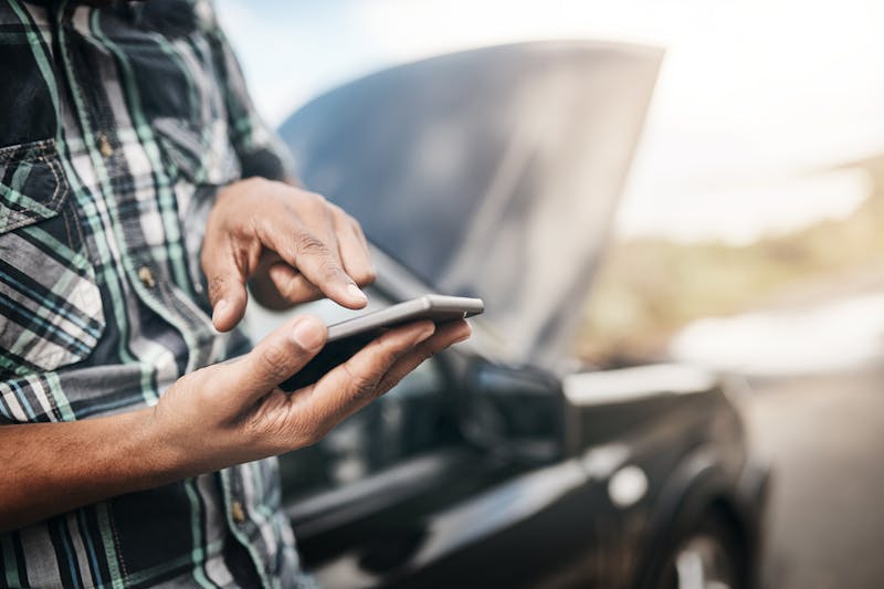 man on his phone with his broken down car on the side of the road