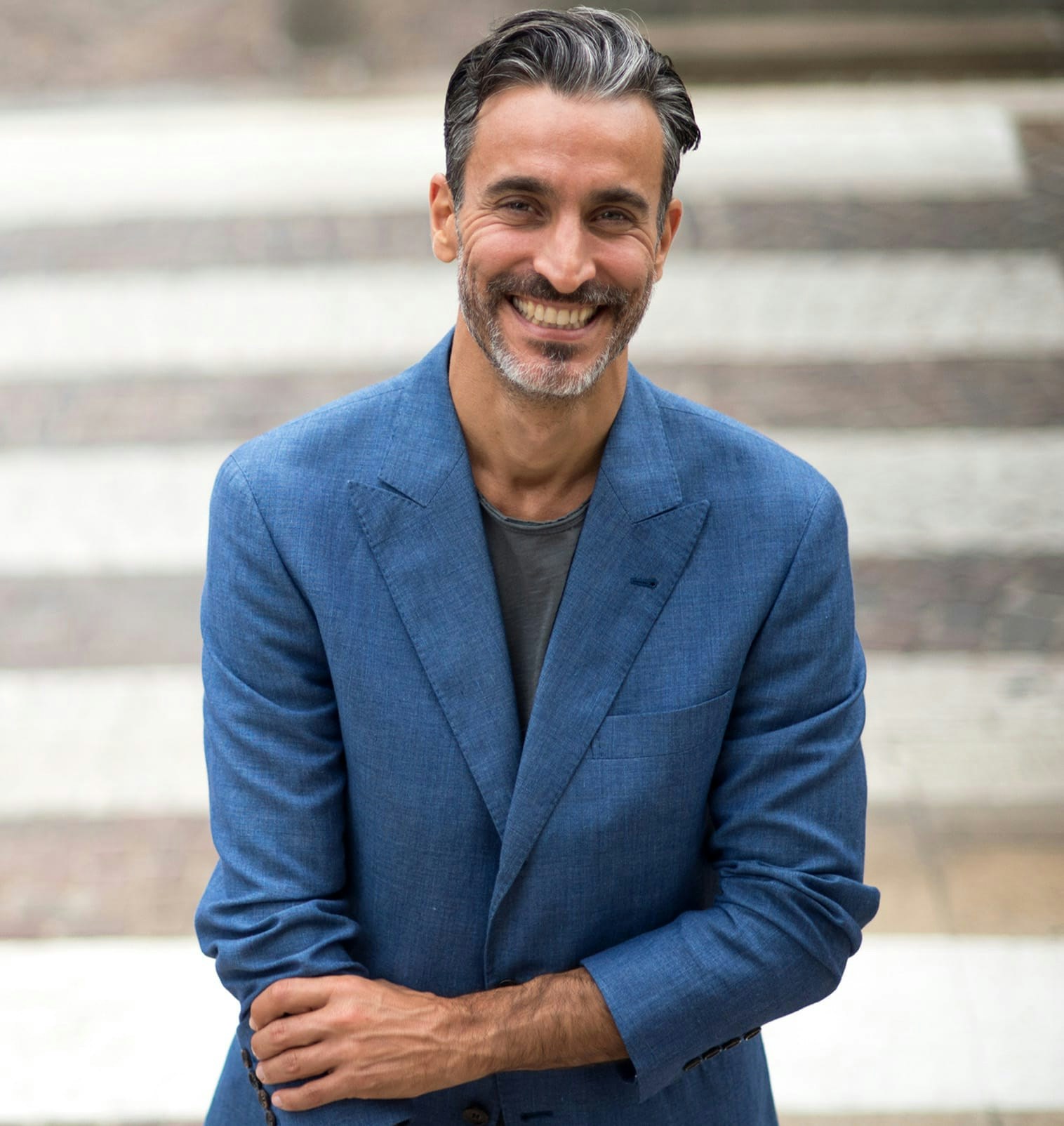 smiling man in blue blazer holding right arm