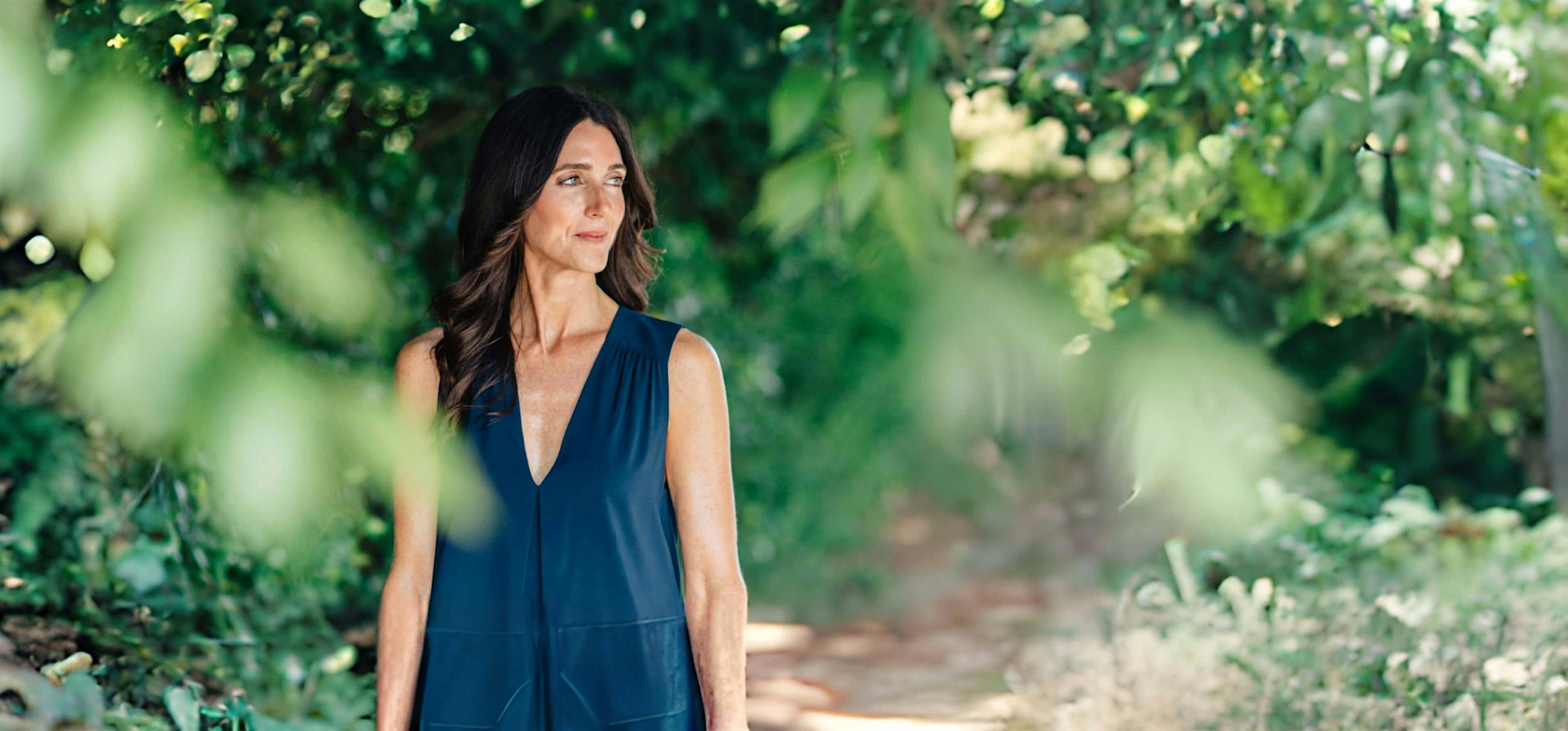 woman in blue blouse looking to left on walking trail