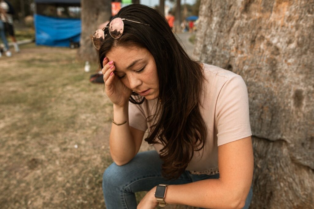 Woman sitting on ground and holding her head in pain