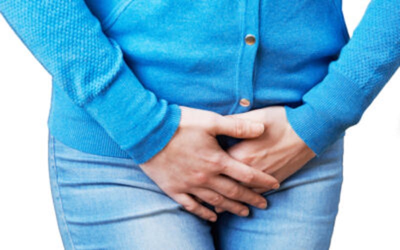 woman in blue sweater and jeans holding her crotch