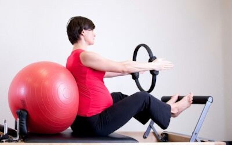 woman sitting on a pilates with a red ball and a wheel