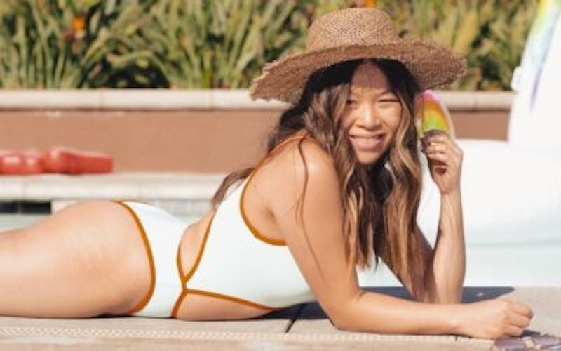 woman in a white bikini and a straw hat laying by the pool