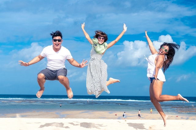 three people smiling and jumping at the beach
