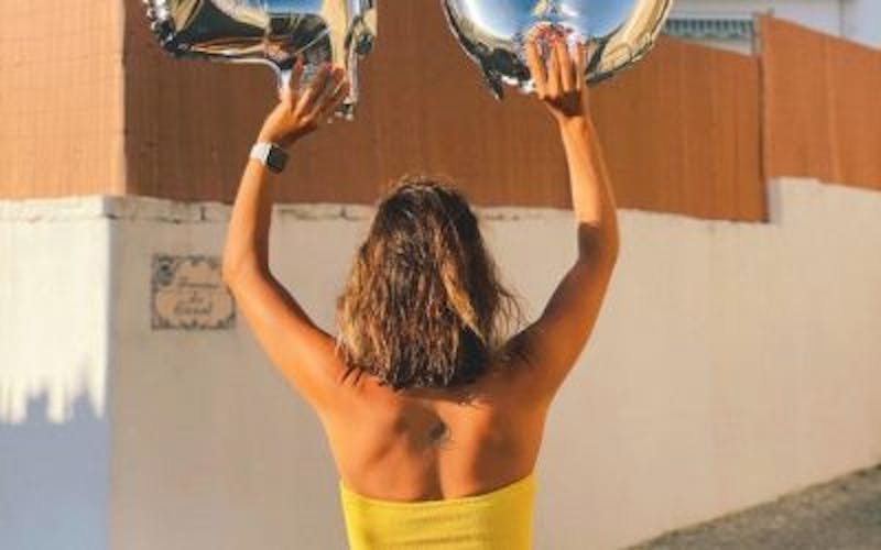 woman in yellow dress holding up two silver balloons
