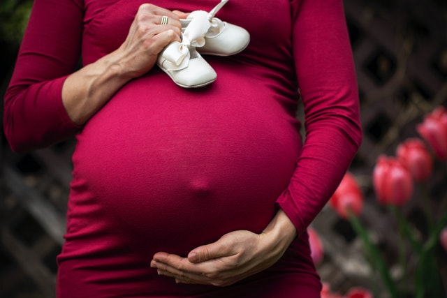 Pregnant woman in red dress holding belly