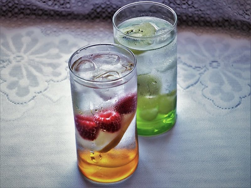 there are two glasses of water with fruit and ice on a table