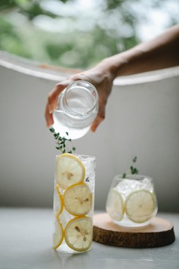 person pouring water into glass full of lemon slices