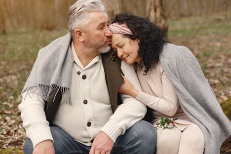older couple sitting near woods and holding each other