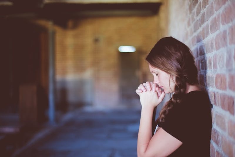 woman standing in front of a brick wall praying