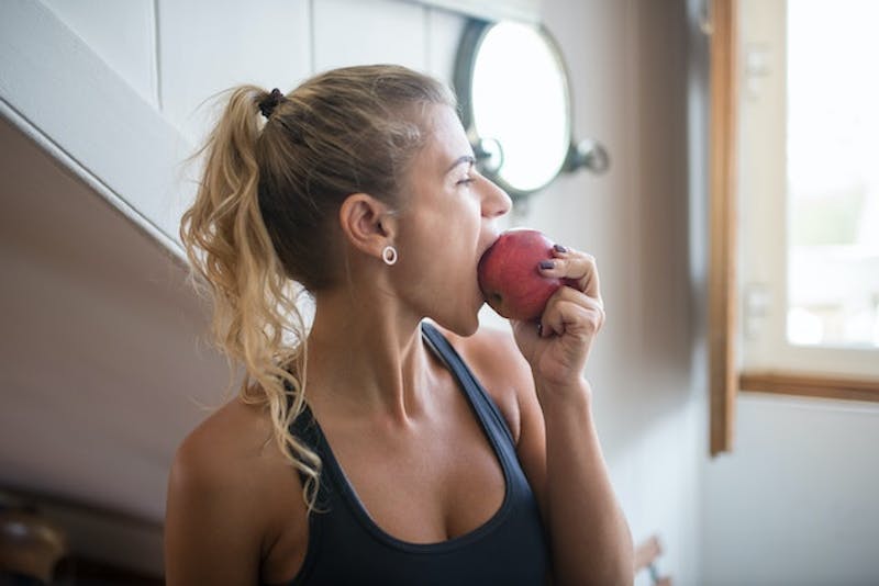 blond woman eating an apple in a kitchen with a window
