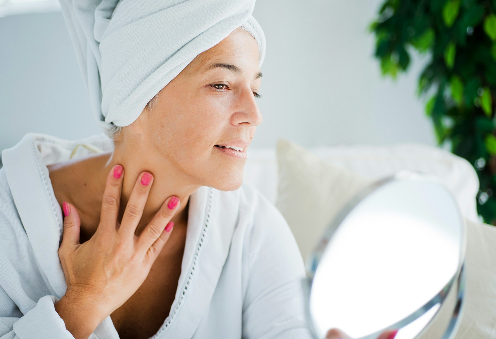 Woman in robe examining her neck in the mirror