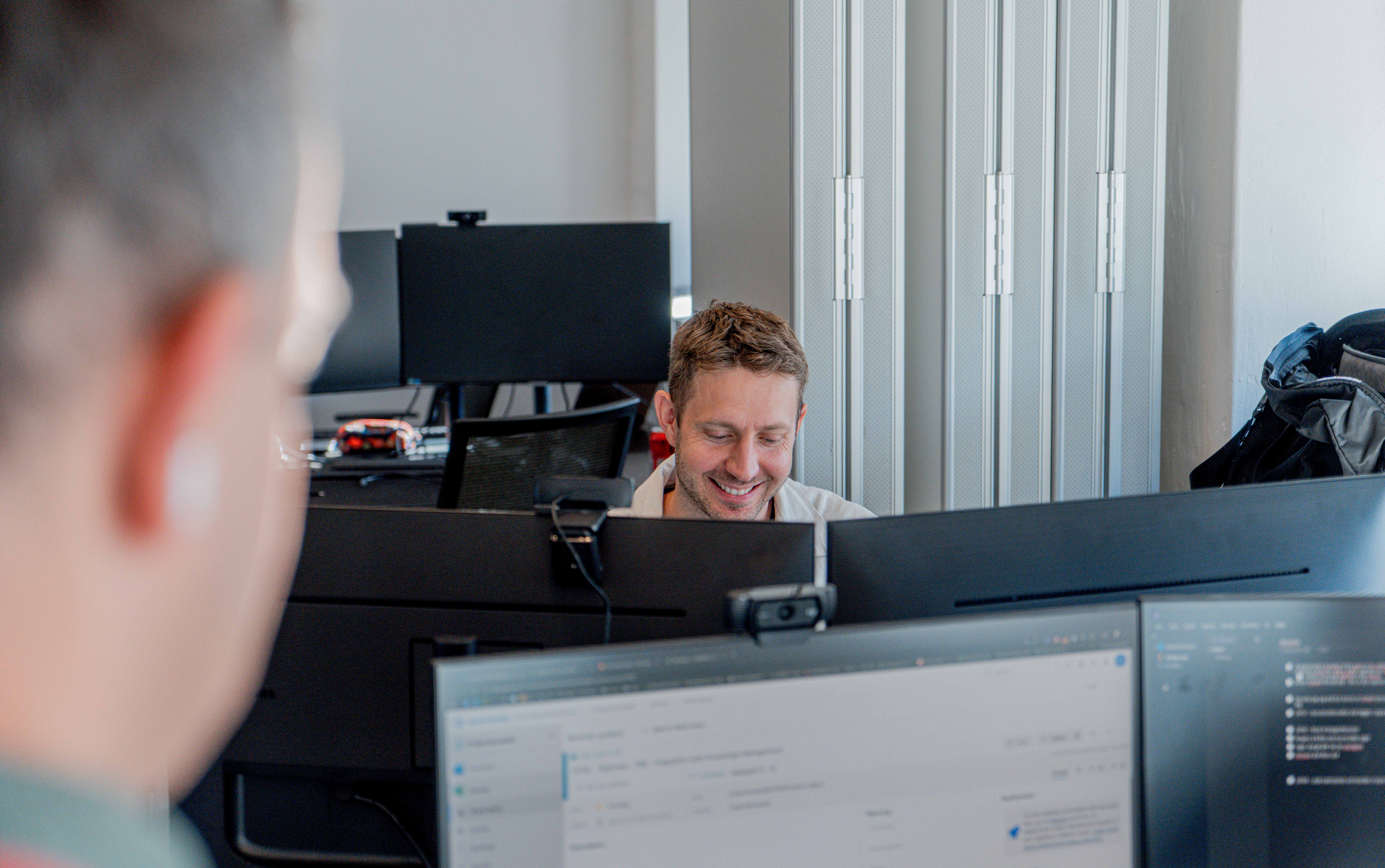 A man smiling while working at a computer in an office for a ServiceNow partner.