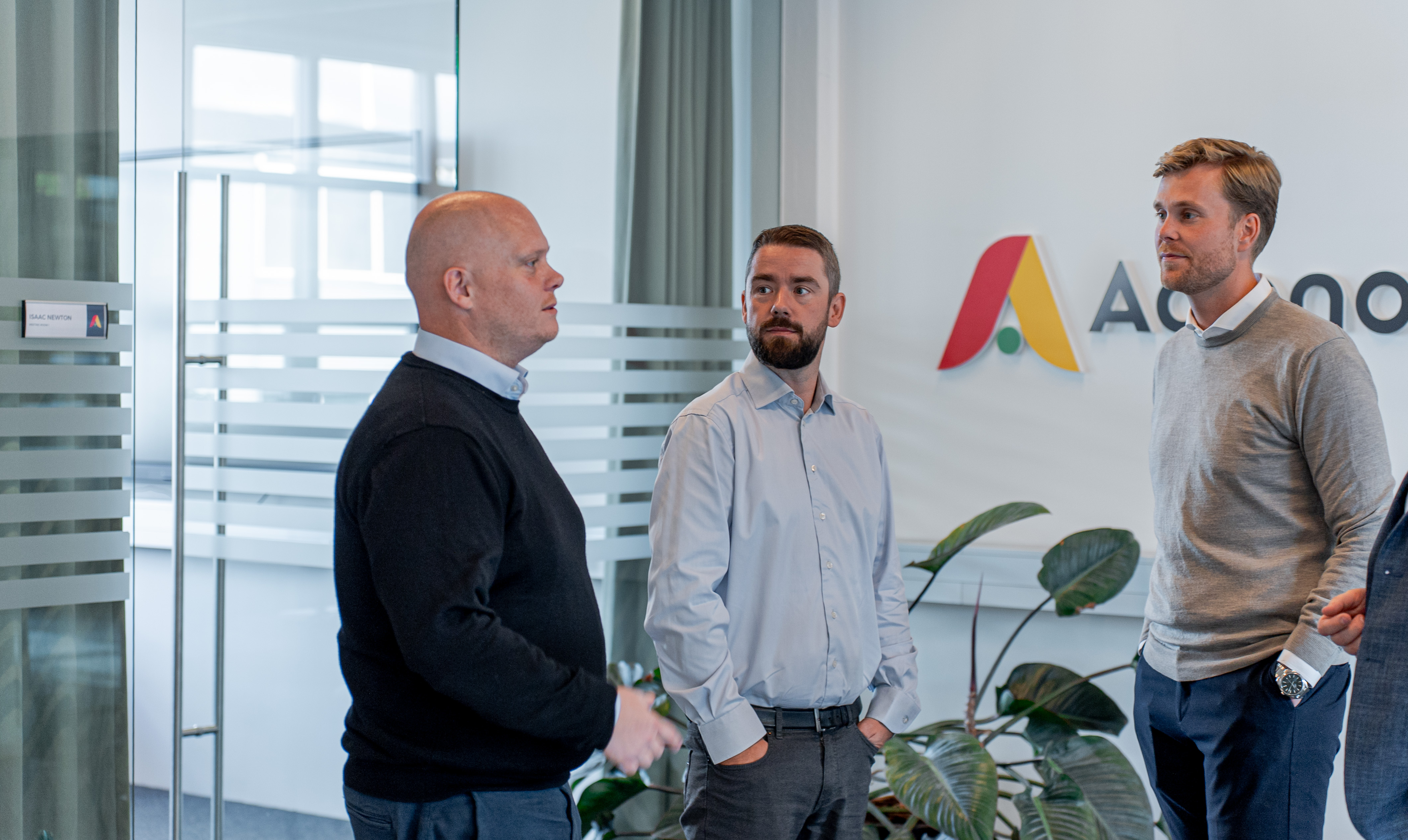 Three men standing and talking in an office at ServiceNow partner Adeno.