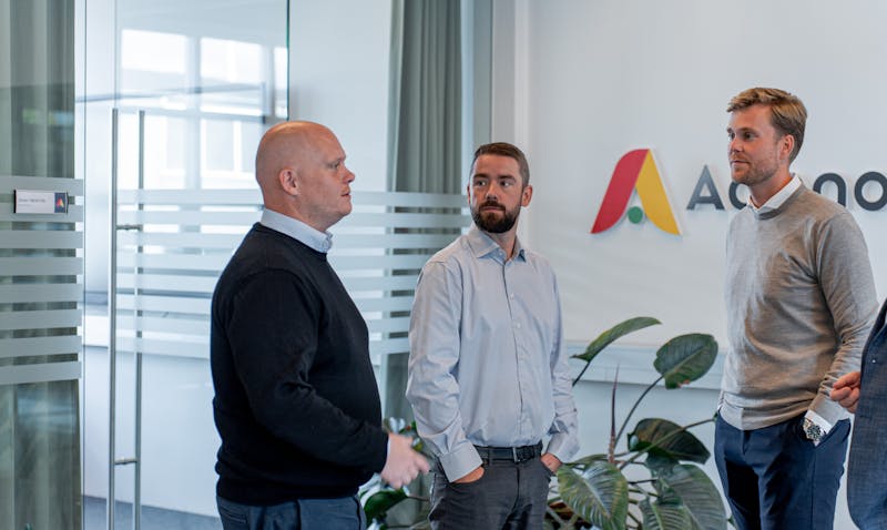 Three men standing and talking in an office at ServiceNow partner Adeno.