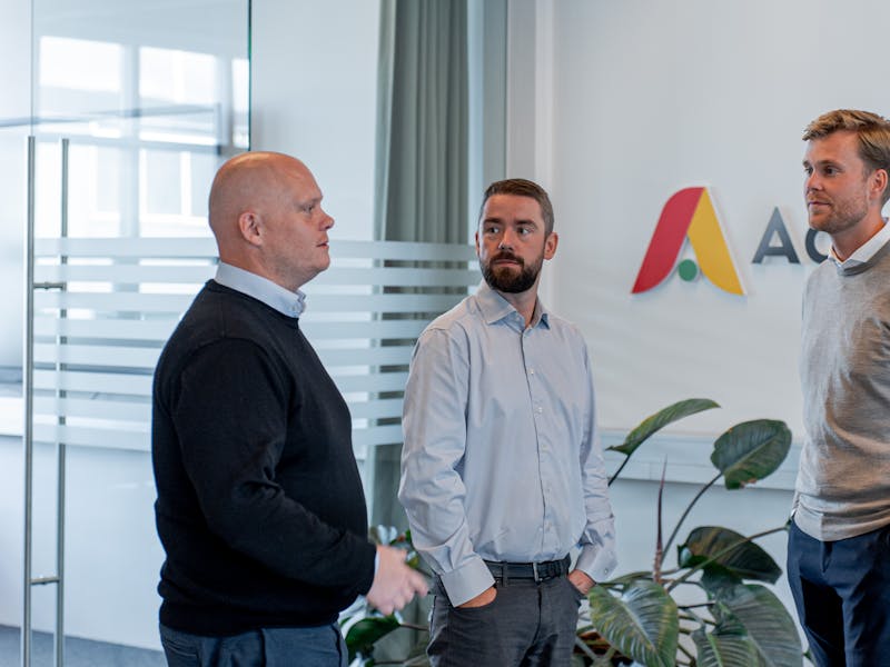Three men standing and talking in an office at ServiceNow partner Adeno.