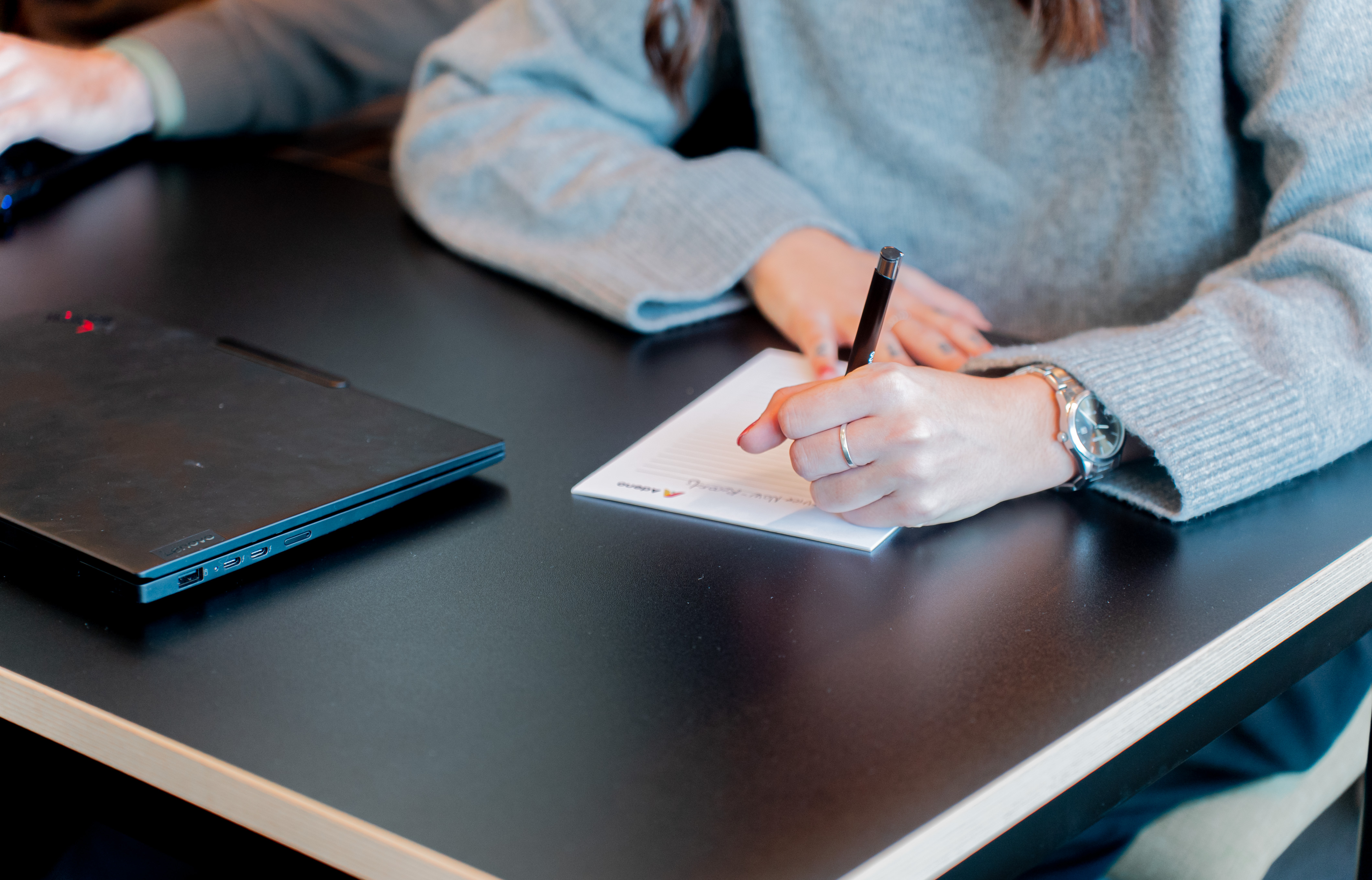 A person writing on a notepad next to a laptop at a ServiceNow partner's office.