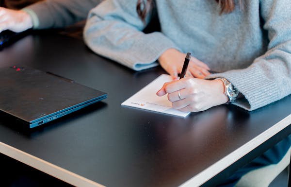 A person writing on a notepad next to a laptop at a ServiceNow partner's office.