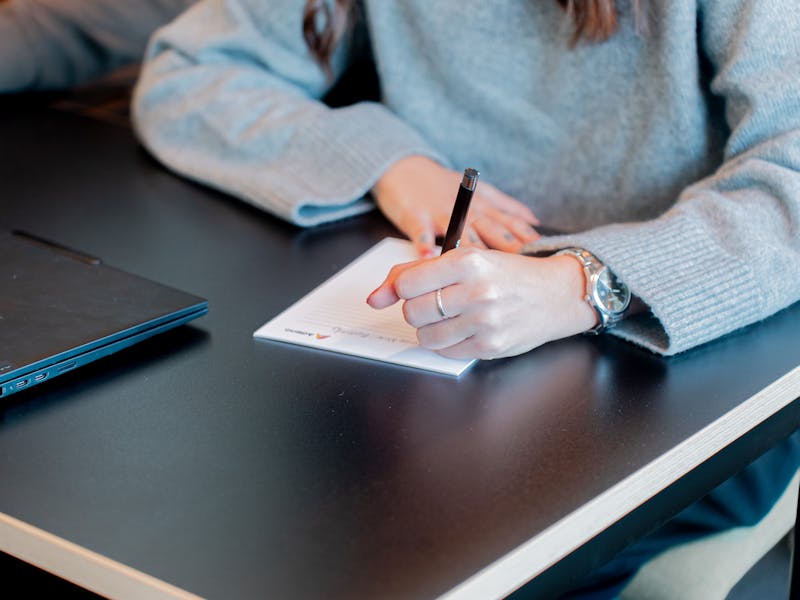 A person writing on a notepad next to a laptop at a ServiceNow partner's office.