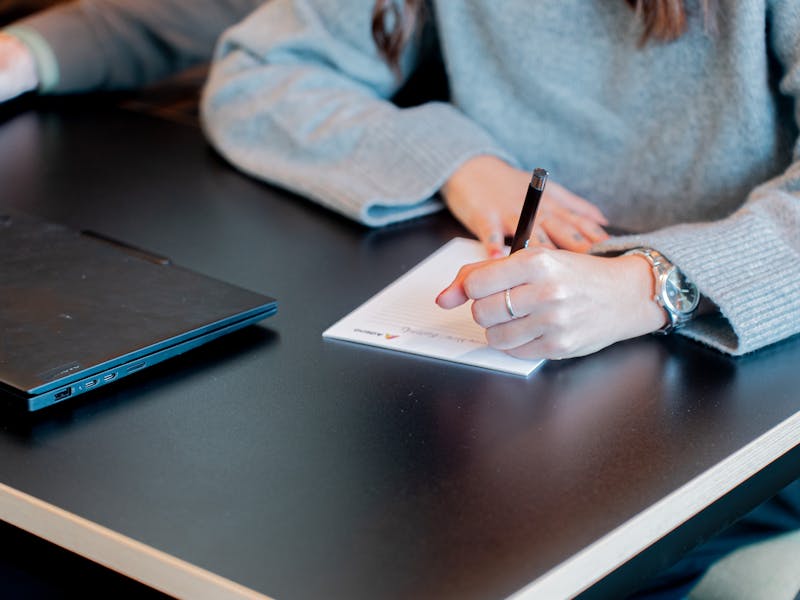 A person writing on a notepad next to a laptop at a ServiceNow partner's office.