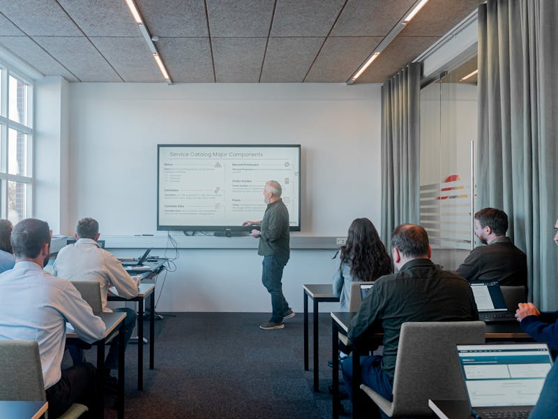 A man presenting a slide titled Service Catalog Major Components about ServiceNow to a group in a classroom.