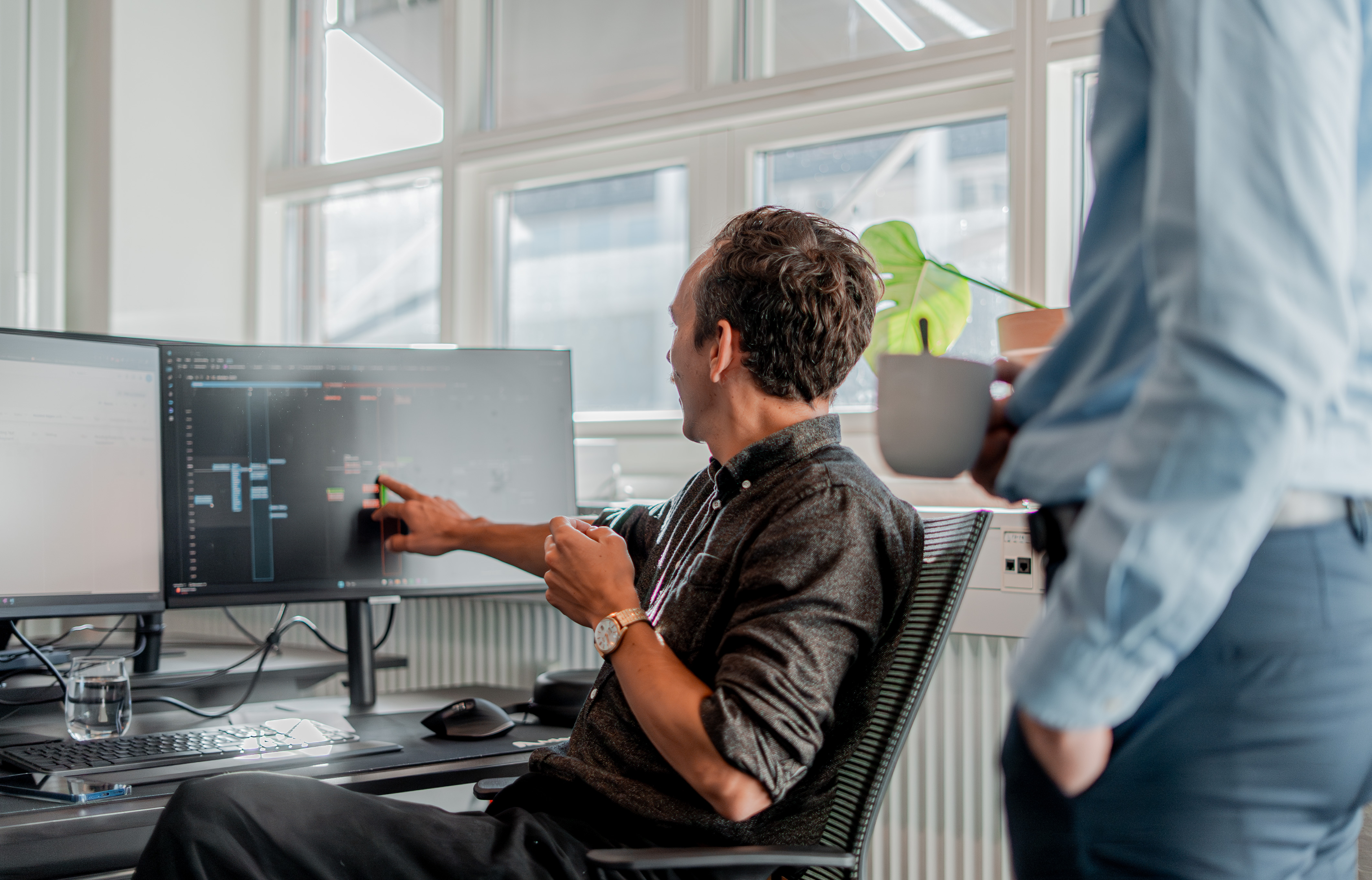 A person at a desk pointing to a computer monitor displaying technical information in a ServiceNow partner office.