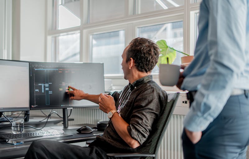 A person at a desk pointing to a computer monitor displaying technical information in a ServiceNow partner office.