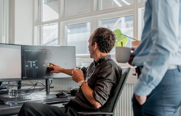 A person at a desk pointing to a computer monitor displaying technical information in a ServiceNow partner office.
