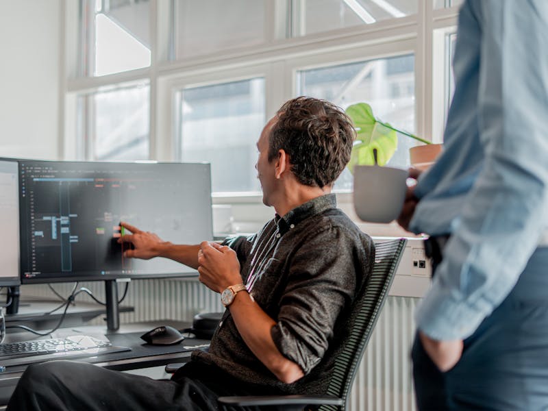 A person at a desk pointing to a computer monitor displaying technical information in a ServiceNow partner office.