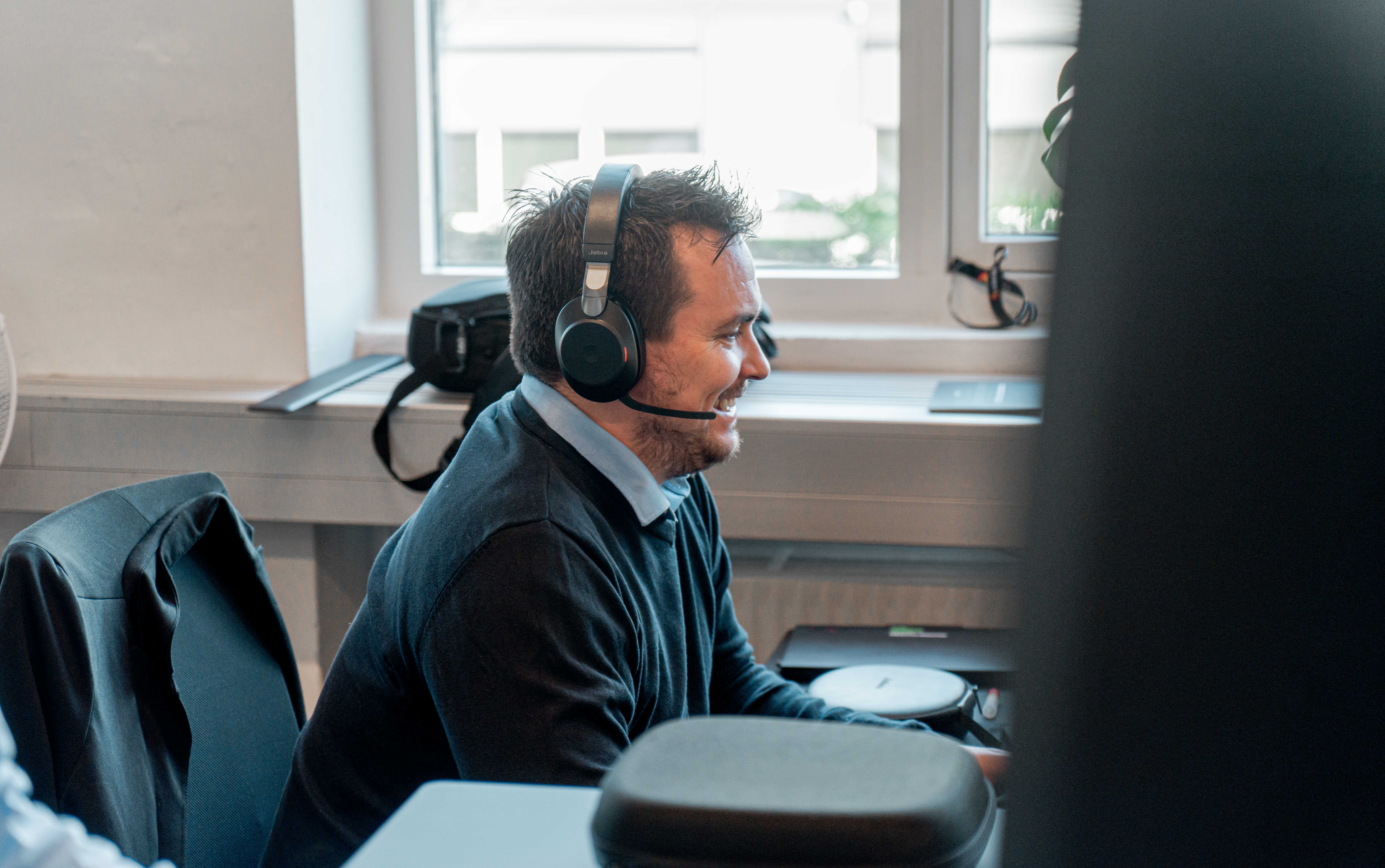 A man wearing a headset and smiling while working at a desk in a ServiceNow partner office.