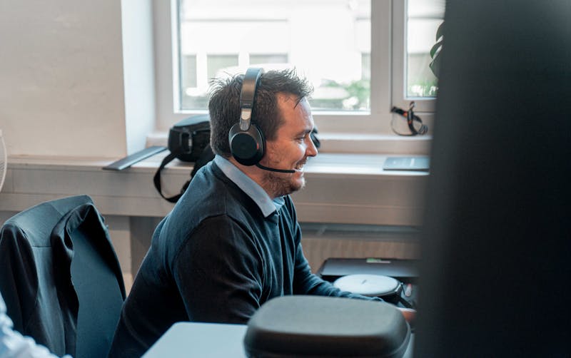A man wearing a headset and smiling while working at a desk in a ServiceNow partner office.