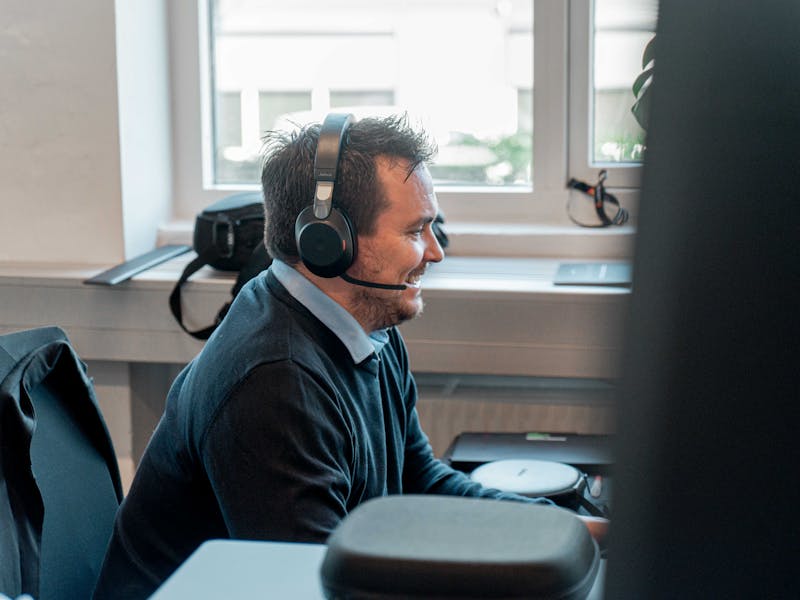 A man wearing a headset and smiling while working at a desk in a ServiceNow partner office.