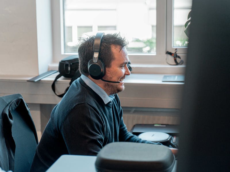 A man wearing a headset and smiling while working at a desk in a ServiceNow partner office.