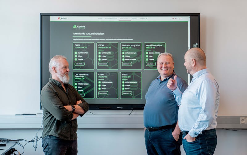 Three men standing in front of a screen displaying a ServiceNow training course schedule.