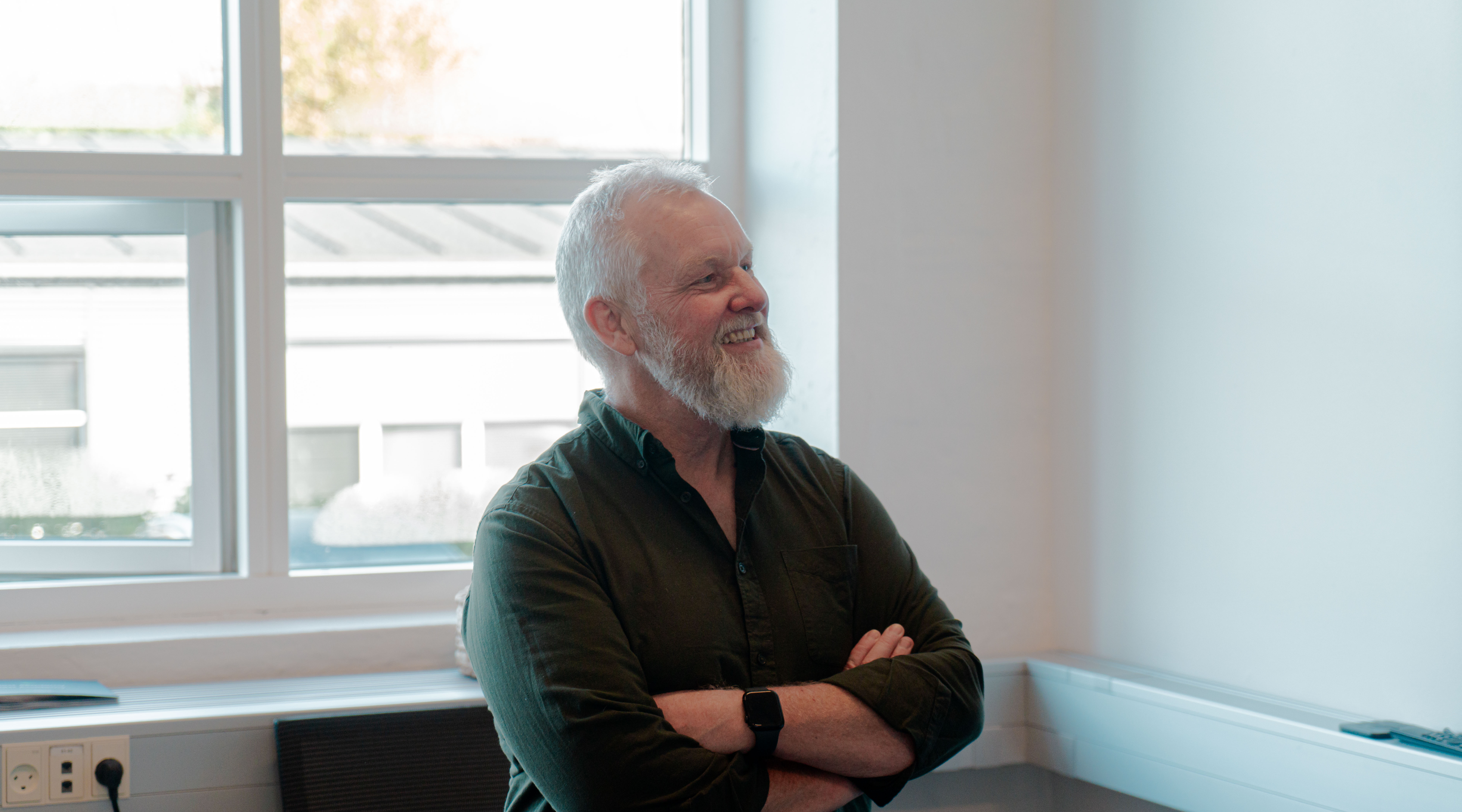 A smiling man with a white beard and crossed arms in an office setting for ServiceNow partner Adeno.