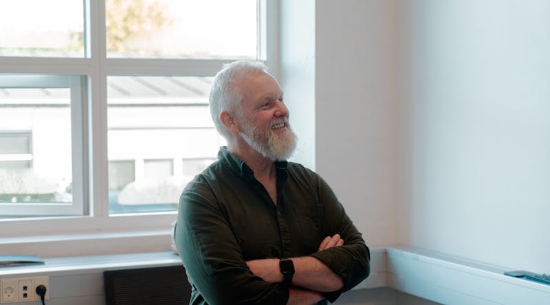 A smiling man with a white beard and crossed arms in an office setting for ServiceNow partner Adeno.