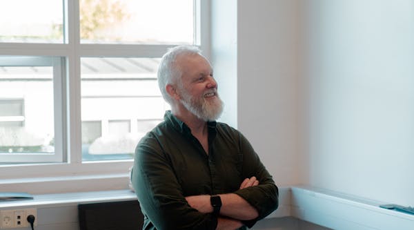 A smiling man with a white beard and crossed arms in an office setting for ServiceNow partner Adeno.